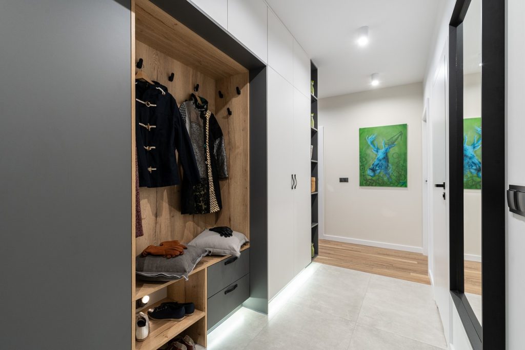 Modern hallway with wooden coat closet, stylish jackets, and vibrant deer artwork on the wall