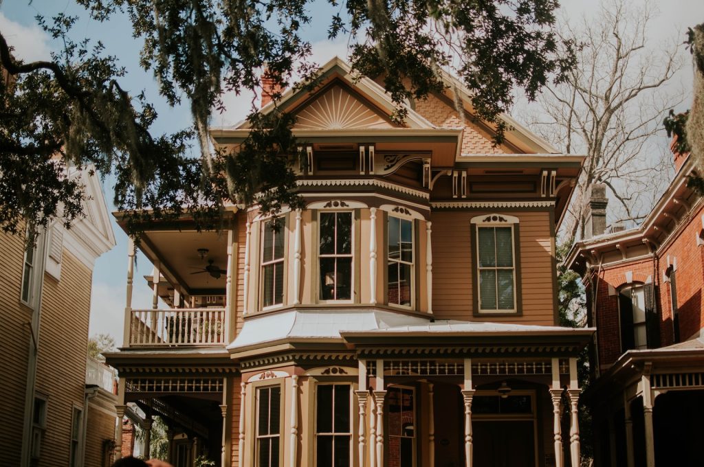 Victorian-style house with ornate woodwork and bay windows under a clear sky, surrounded by trees